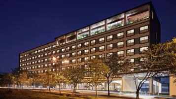 Um hotel moderno com vários andares, grandes janelas e fachada bem iluminada.