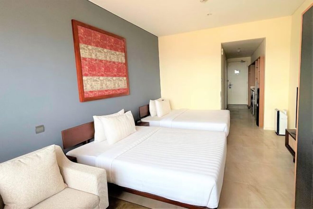 A hotel room with two beds, a sofa, a large abstract painting, and a hallway leading to other rooms.