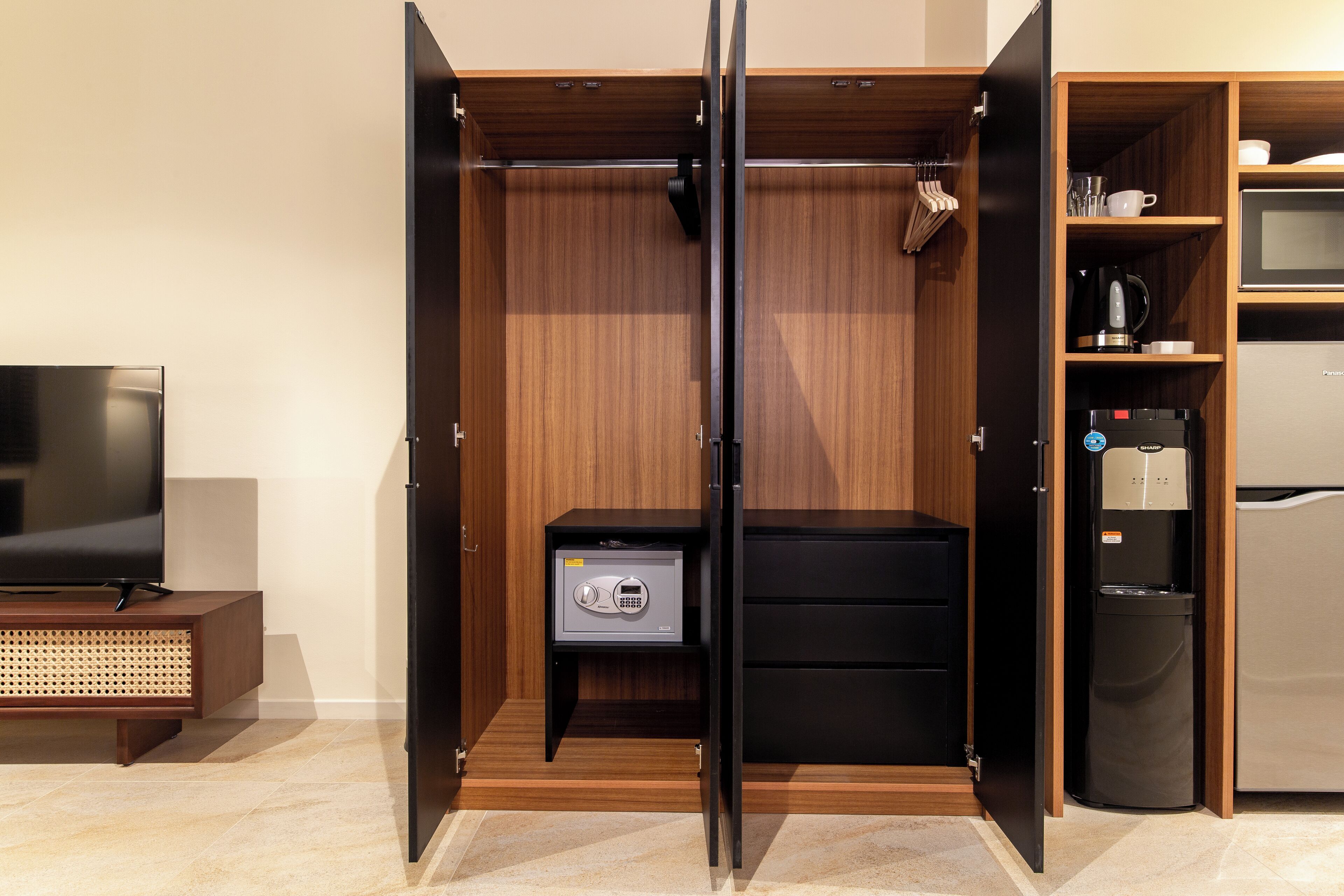 Una habitación moderna con televisión, caja fuerte, dispensador de agua y microondas.
