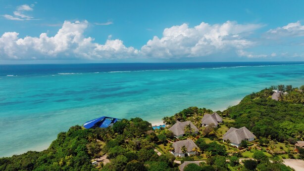 Un resort tropical con cabañas de techo de paja, una playa y una vista despejada del mar turquesa.