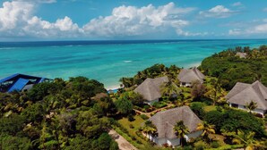 Un resort tropical con cabañas de techo de paja, exuberante follaje y vista al mar turquesa.
