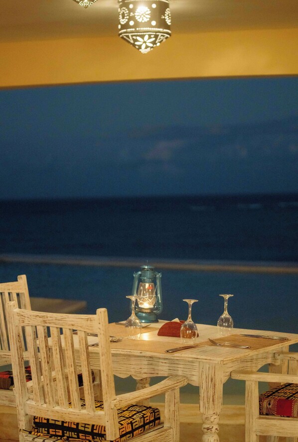 A dining table with chairs and a candle, set against a view of the ocean.