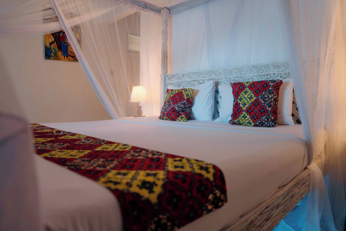Ein Bett mit Baldachin, einer gemusterten Tagesdecke und zwei Kissen mit floralem Muster.
