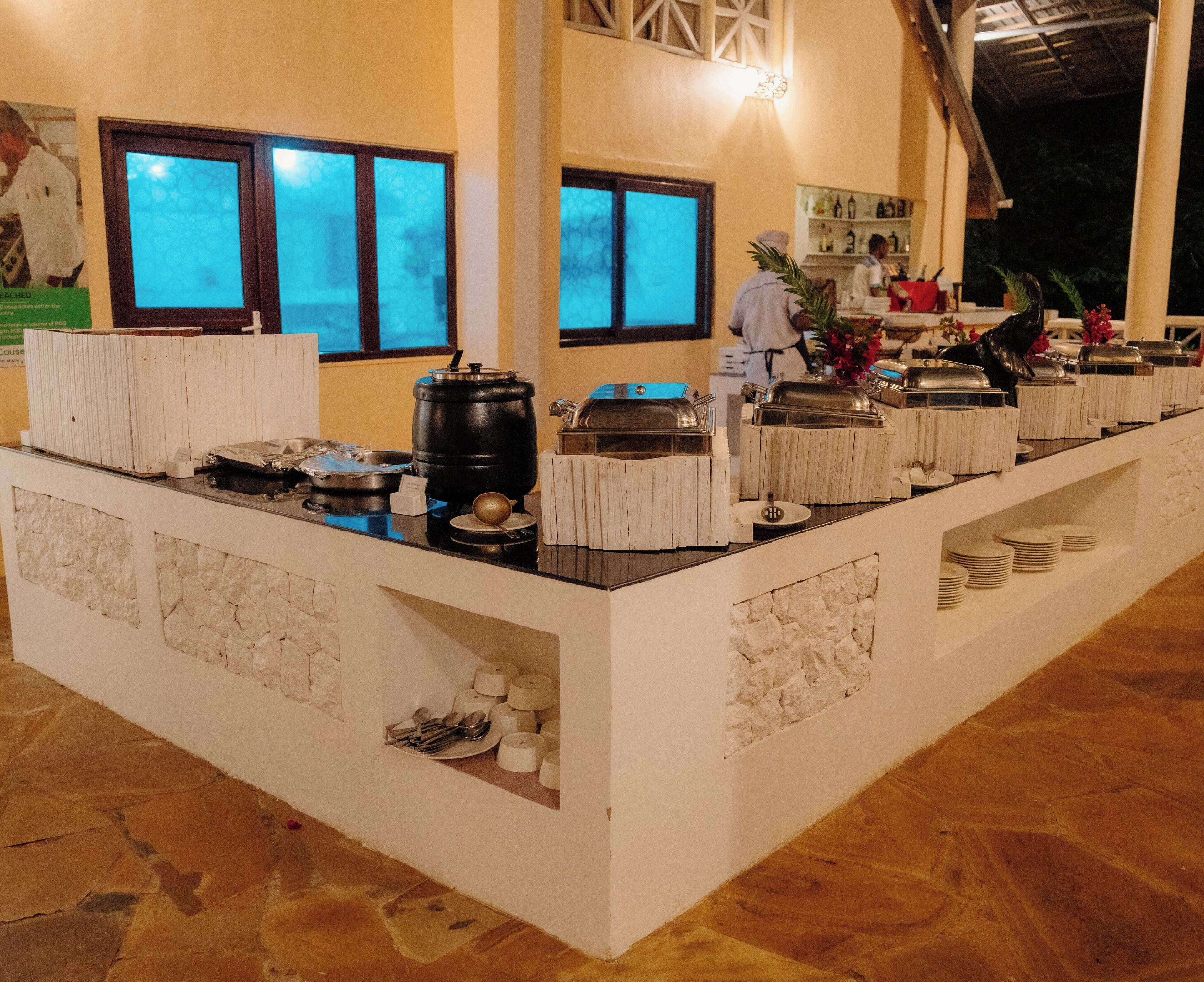 A buffet setup with various food stations, a coffee machine, and a bar area in a hotel setting.