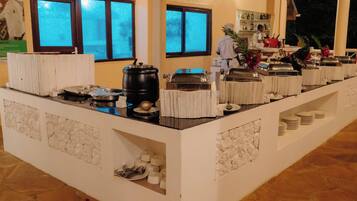 A buffet setup with various food stations, a coffee machine, and a bar area in a hotel setting.