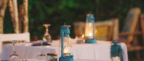Un tavolo da pranzo all'aperto apparecchiato con candele, bicchieri e un menu.