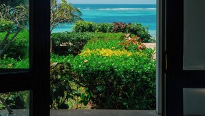 Vista desde una habitación a través de una puerta abierta, mostrando un balcón con abundante vegetación y una vista despejada del océano.