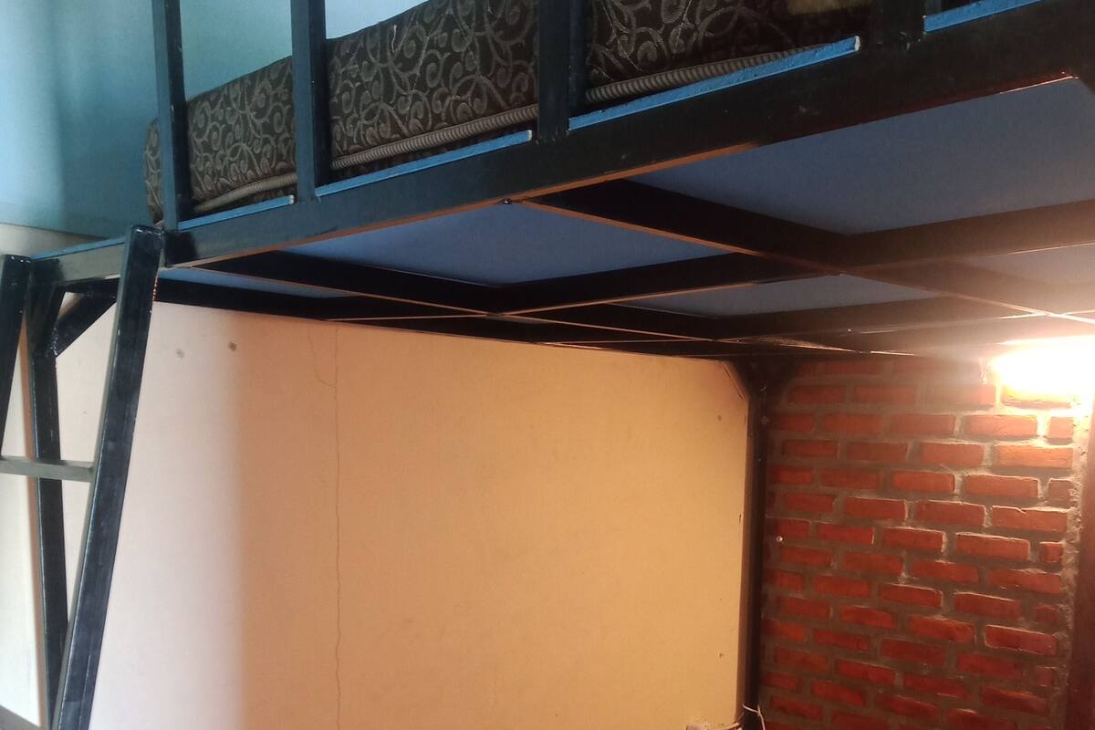 Een kleine kamer met een stapelbed, een bakstenen muur en een raam.
