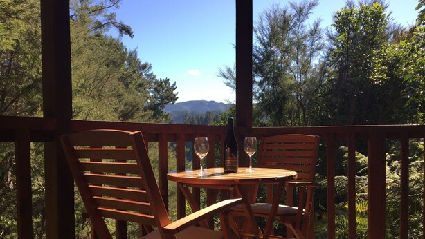 A wooden deck with two chairs and a table, a bottle of wine, and a glass on the table. - Kanuka Ridge Lodge and Backpackers (Kaiteriteri)