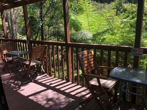 Une terrasse en bois avec un espace salon extérieur, comprenant des chaises et une table, entourée d’une végétation luxuriante et de fougères.
