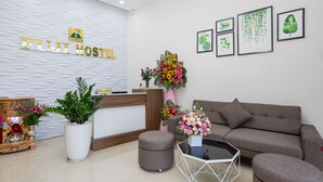 A FUJI HOSTEL recepciója egy pulttal, egy kanapéval, egy kávézóasztallal és egy virágtartóban elhelyezett növényekkel van berendezve.