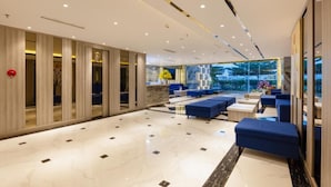 A modern lobby with a marble floor, blue seating area, and large windows offering a view. - Ruby Luxury Hotel (Nha Trang)