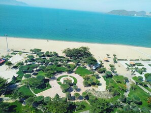 An aerial view of a coastal resort with manicured gardens, a sandy beach, and a clear view of the sea. - Ruby Luxury Hotel (Nha Trang)