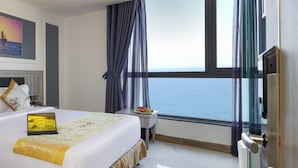 A hotel room with a bed, a laptop, a small table with fruit, and a view of the sea through large windows. - Ruby Luxury Hotel (Nha Trang)