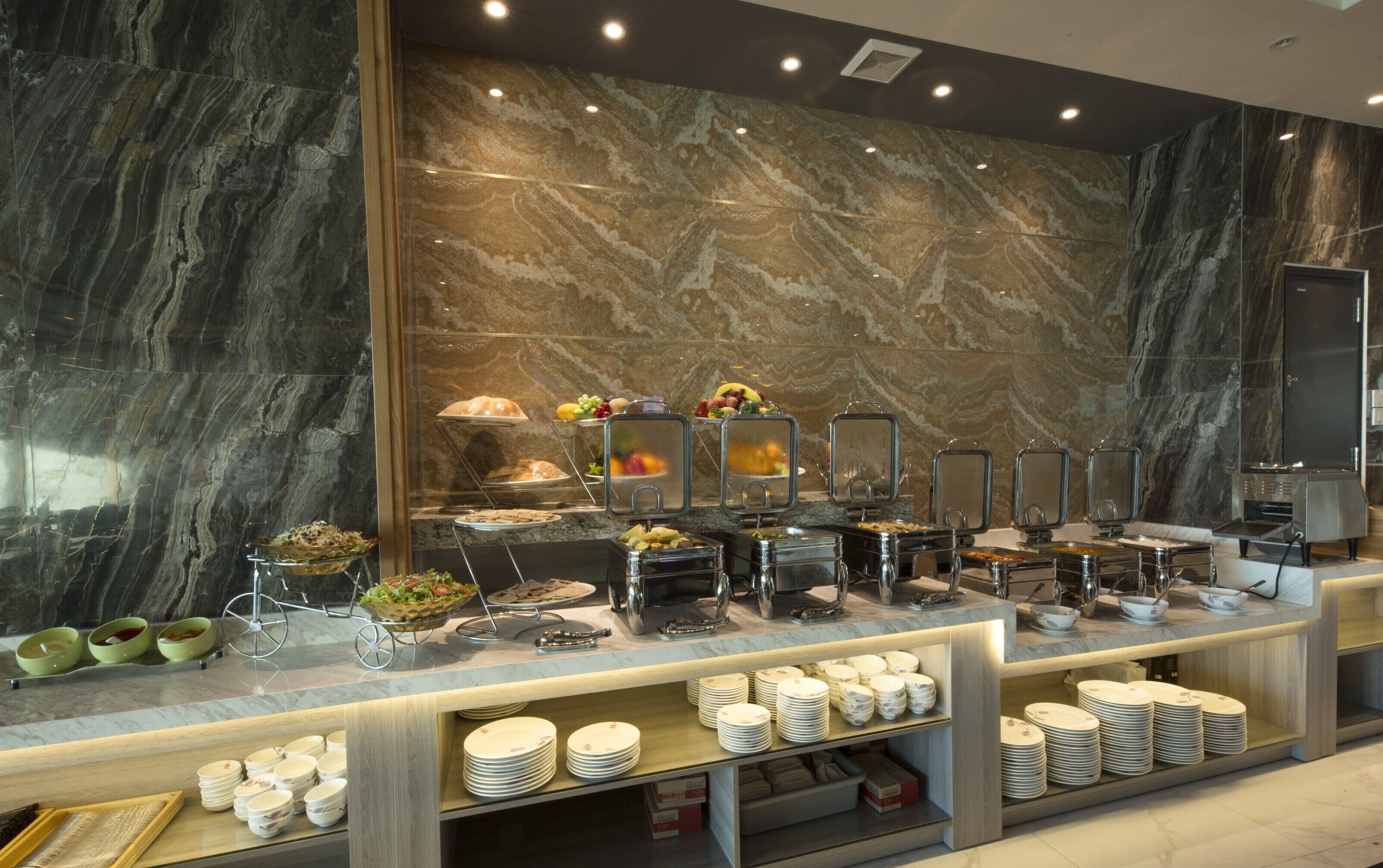 A buffet setup with various food stations and a marble wall background.