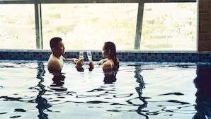 A couple in a swimming pool with a view of a cityscape through large windows. - Ruby Luxury Hotel (Nha Trang)