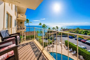 A balcony with a pool, overlooking a parking area and a beach.