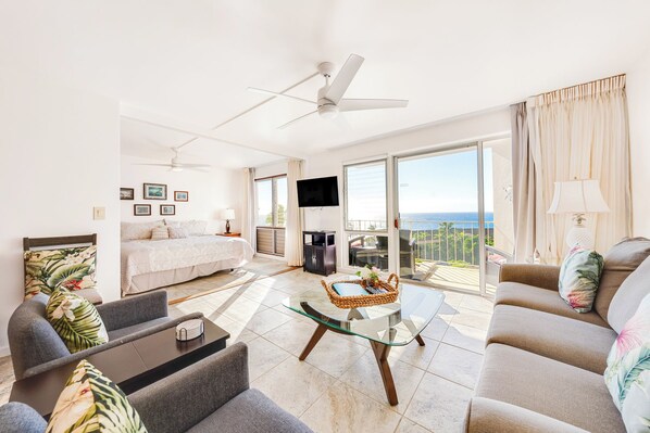 A spacious living room with a bed, a glass coffee table, and a balcony with a view.