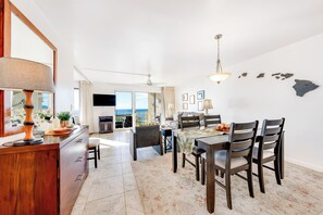 A spacious living area with a dining table, chairs, and a view of the ocean.