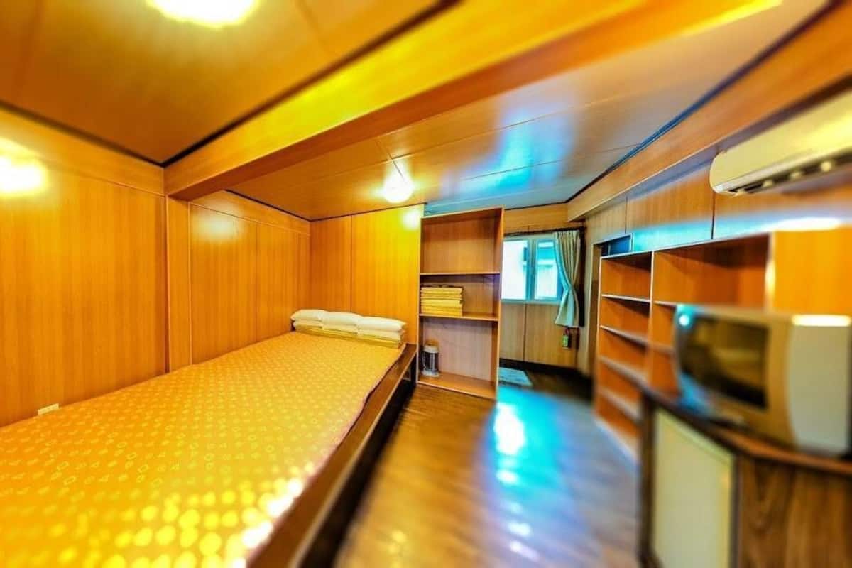 A compact, wooden-furnished cabin with a single bed, a small kitchenette, and a window.