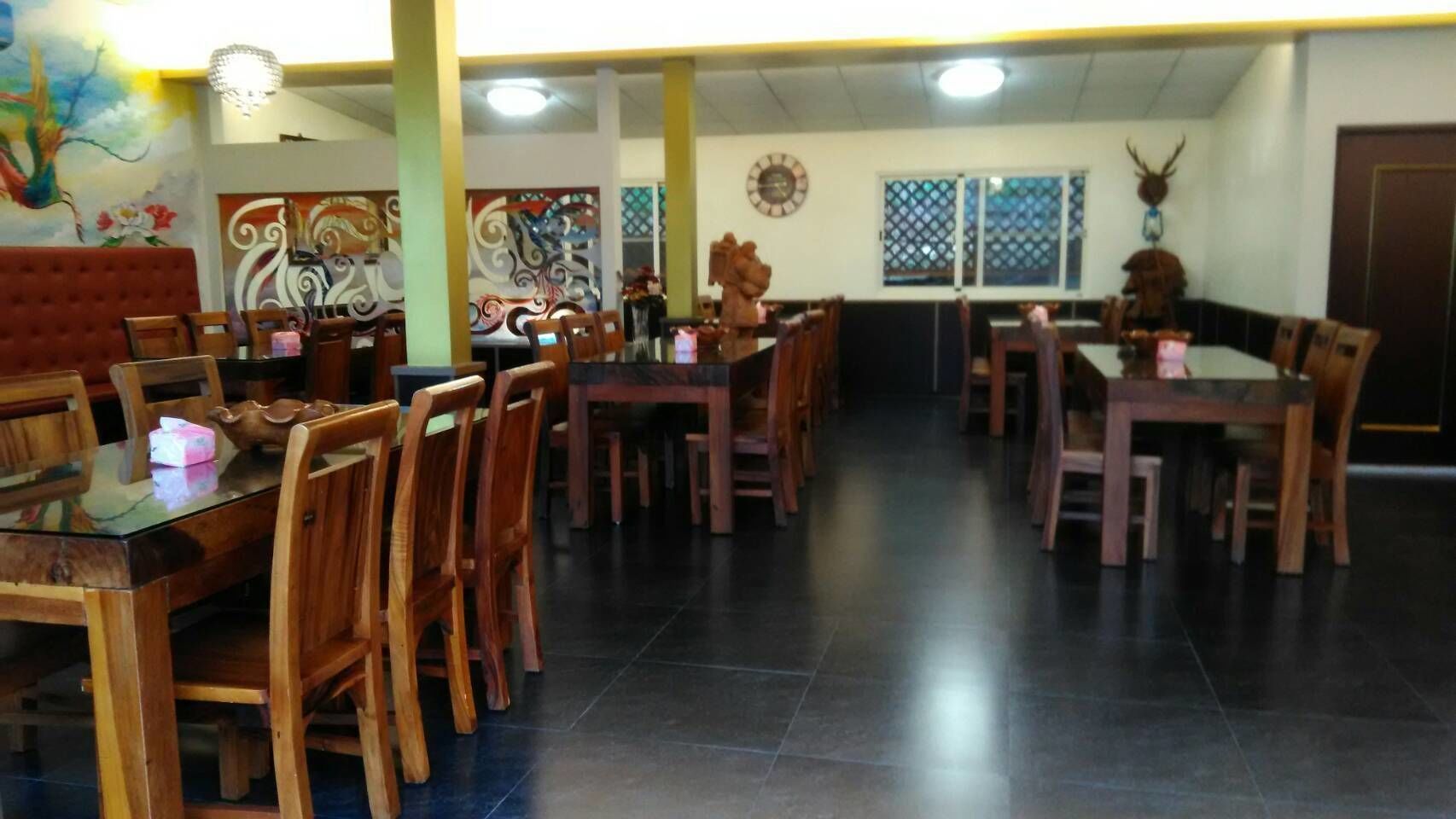 Un espace repas comprenant plusieurs tables et chaises en bois, une horloge au mur et un élément décoratif mural.
