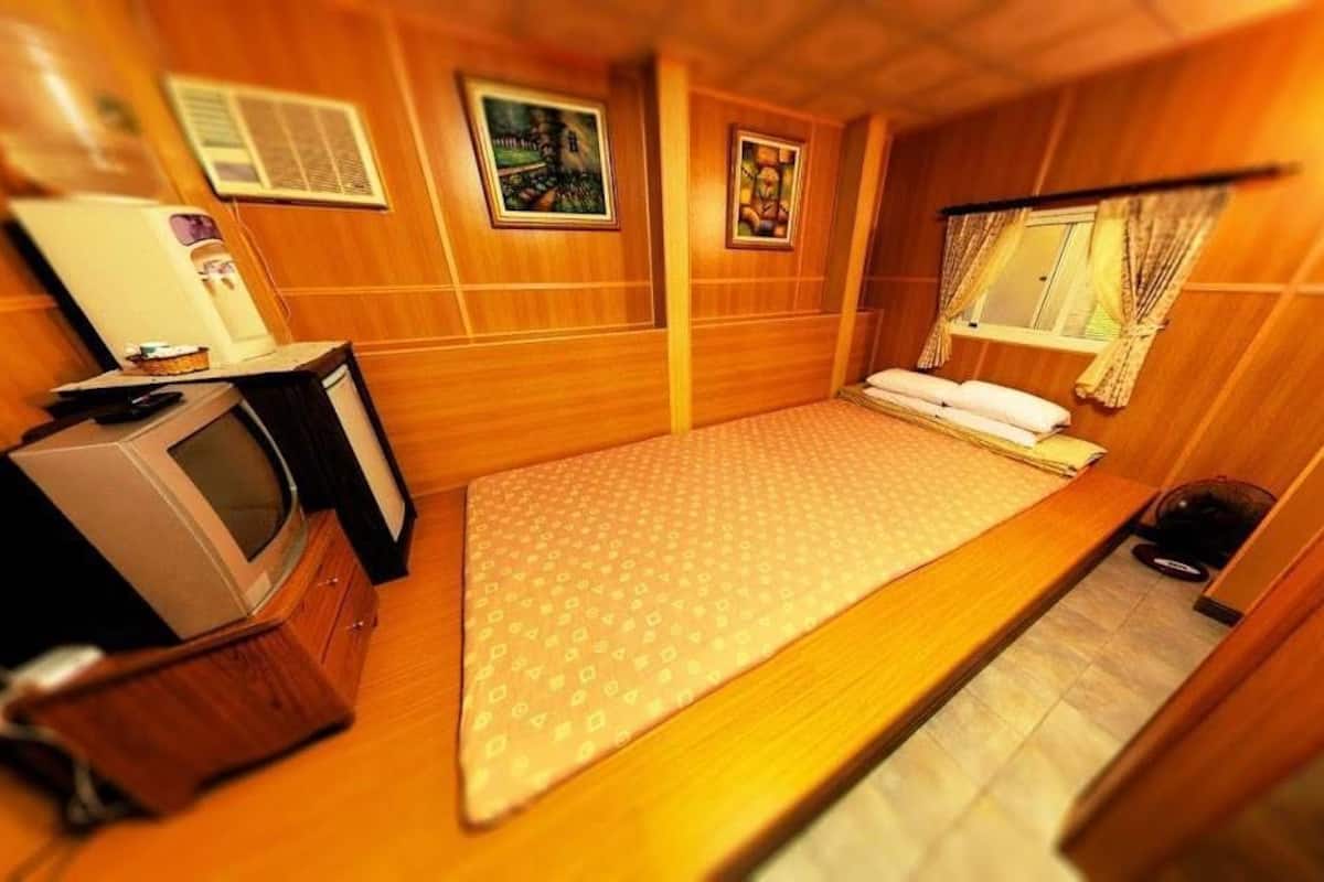 A compact room with a bed, a small desk with a television, and a window with curtains.