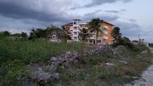 Un immeuble à plusieurs étages doté de balcons, entouré de végétation et bordé d’un terrain rocheux.