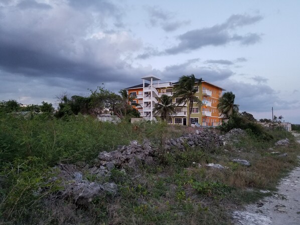 Un edificio de varios pisos con balcones, rodeado de vegetación y un primer plano rocoso.