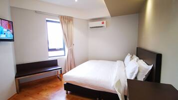 Ein Hotelzimmer mit einem Bett, einer Sitzbank, einem Schreibtisch, einem Fenster mit Vorhängen und einer Klimaanlage.