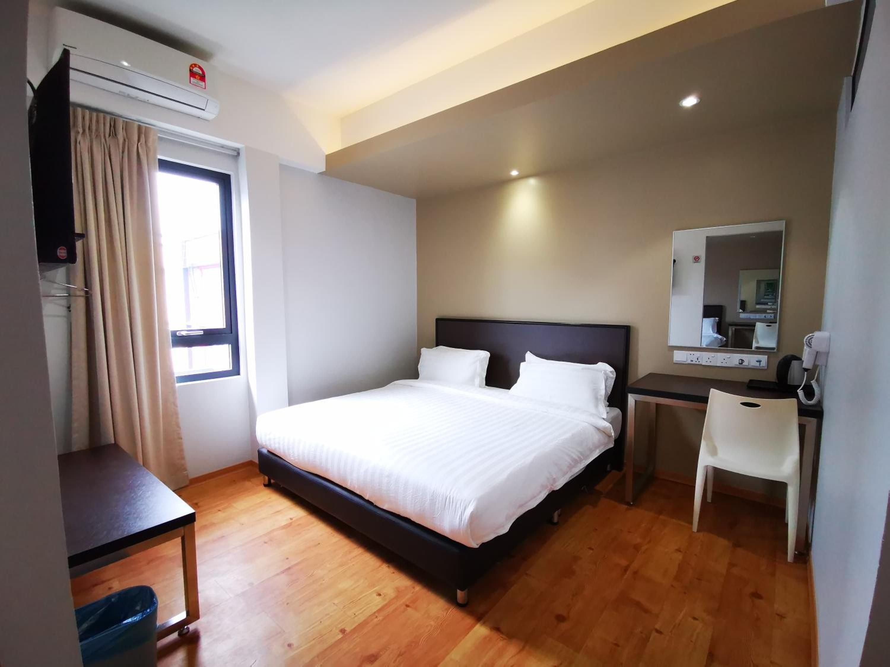 A hotel room with a bed, a desk, a chair, a mirror, and a window with curtains.