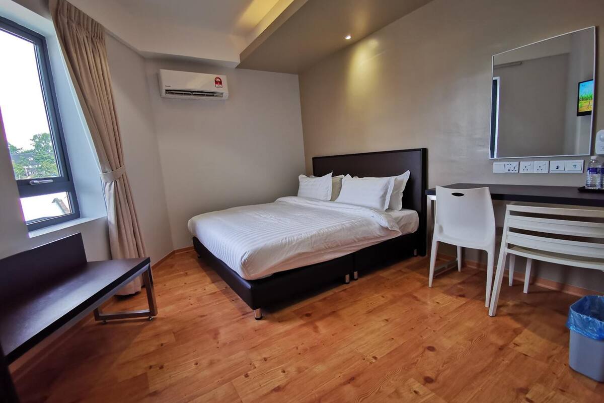 A bedroom with a bed, a desk, a chair, an air conditioning unit, and a window with curtains.