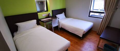Hotelkamer met twee bedden, een bureau, een stoel, een kleine tafel, een spiegel, een raam met gordijnen en een prullenbak.