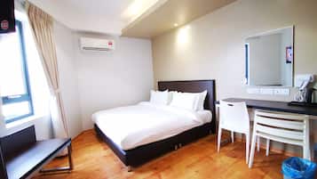 A hotel room with a bed, desk, chair, and a trash bin.