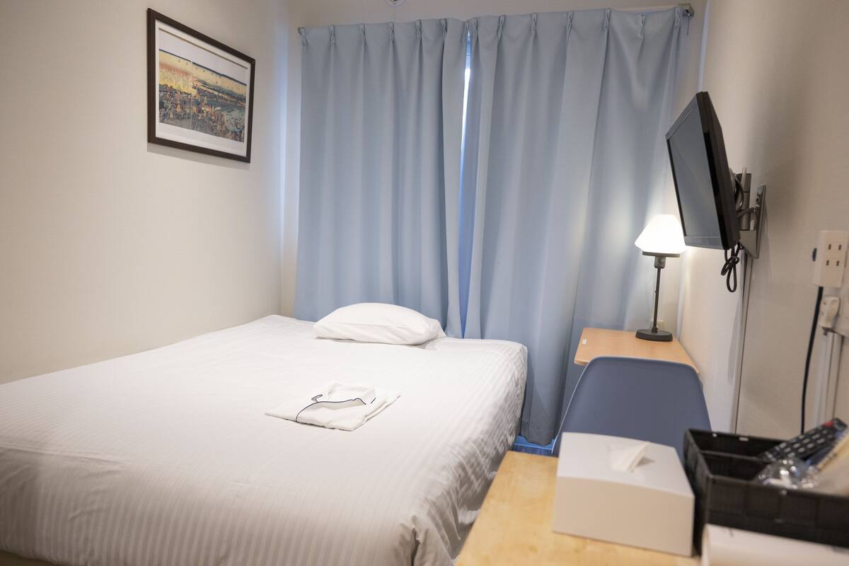 Une chambre d’hôtel avec un lit, un bureau doté d’une lampe, une télévision et une fenêtre avec des rideaux.