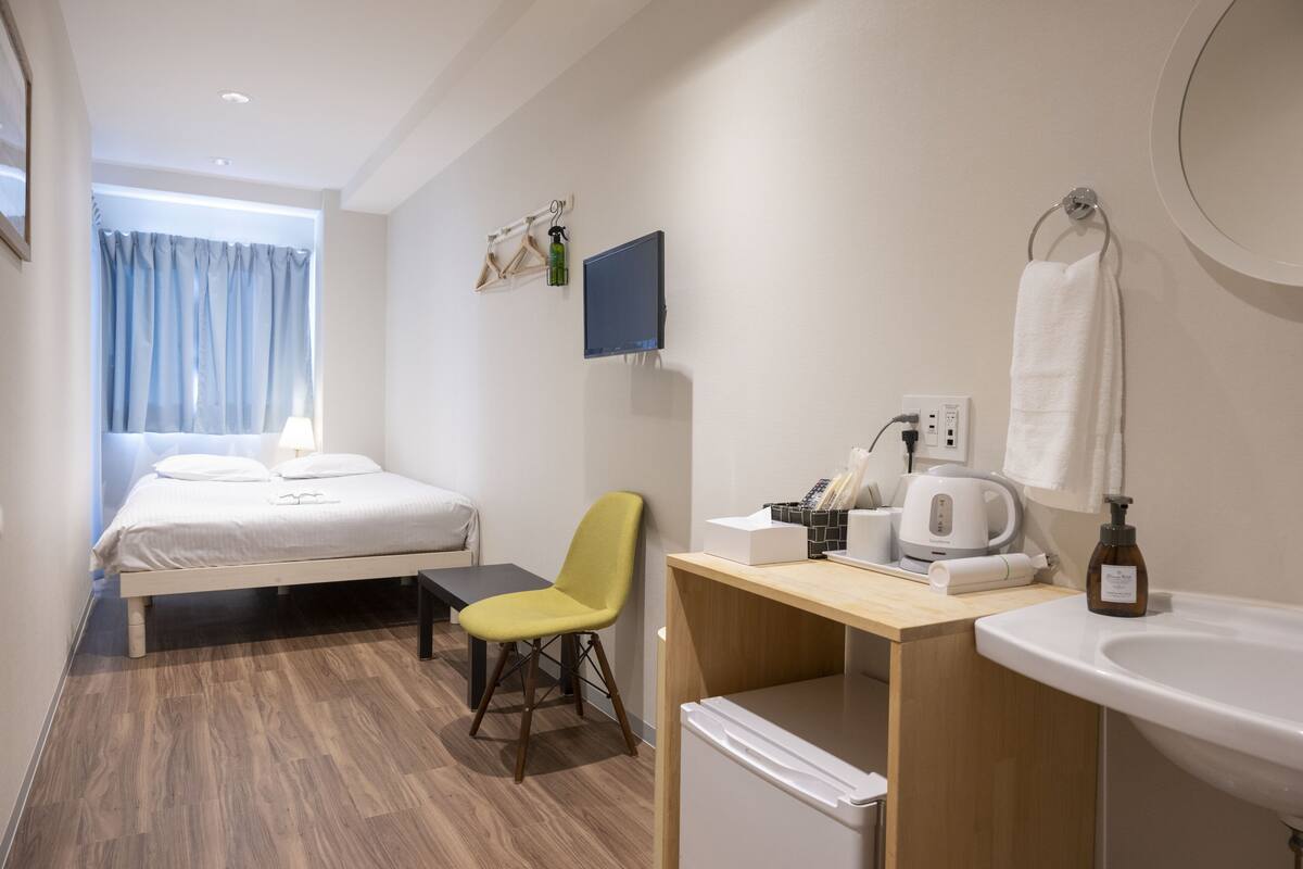 Une chambre d’hôtel comprenant un lit, un bureau, une chaise, un lavabo, un miroir, une télévision et une fenêtre avec des rideaux.