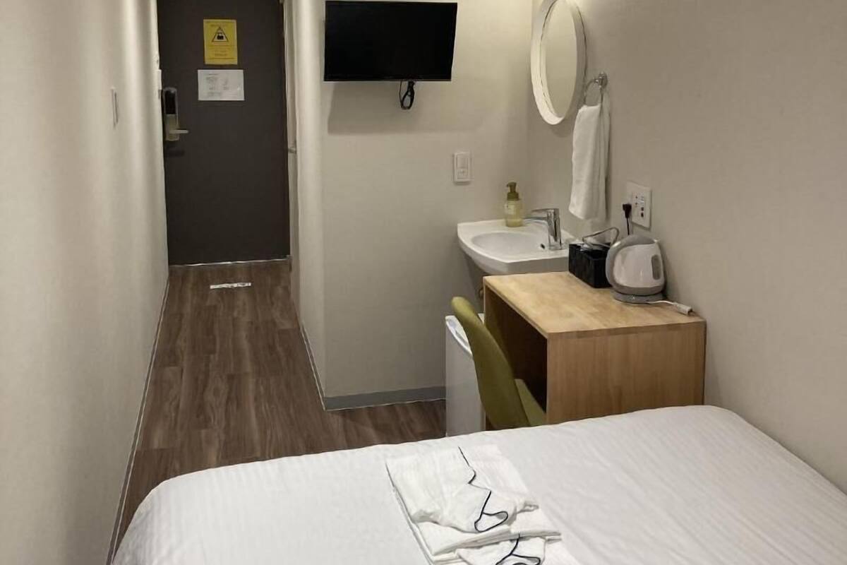Une chambre d’hôtel équipée d’un lit, d’un bureau avec une chaise, d’un lavabo, d’un miroir et d’un téléviseur fixé au mur.