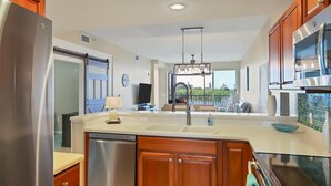 A modern kitchen with a large island, stainless steel appliances, wooden cabinets, and a view to the outdoors.
