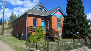 A two-story brick building with a blue and pink roof, a wooden staircase, and a stone fence. - Cripple Creek Beauty  (Cripple Creek)