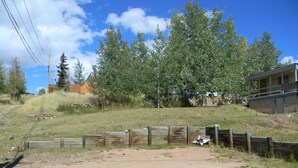 A grassy area with a wooden fence, trees, and a building in the background. - Cripple Creek Beauty  (Cripple Creek)