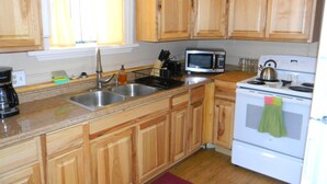 A kitchen with wooden cabinets, a stainless steel sink, a microwave, a stove, and a window with curtains. - Cripple Creek Beauty  (Cripple Creek)