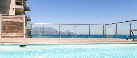A clear blue pool with a view of the ocean and a mountain in the distance.