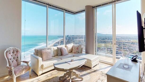 A spacious living room with a large window overlooking a cityscape and the ocean. - Horizon Bay 1604 (Cape Town)