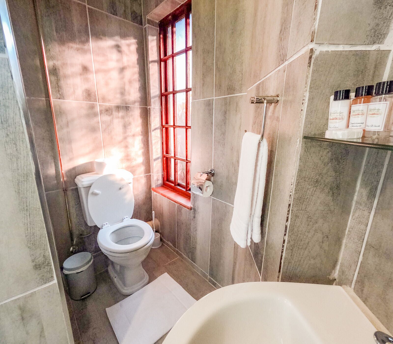 A bathroom with a toilet, a bathtub, and a window with red framing.