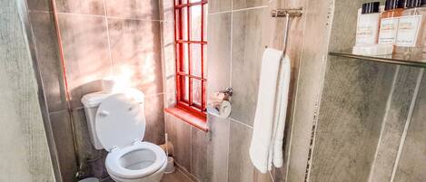 Un baño con inodoro, bañera y ventana con detalles rojos.