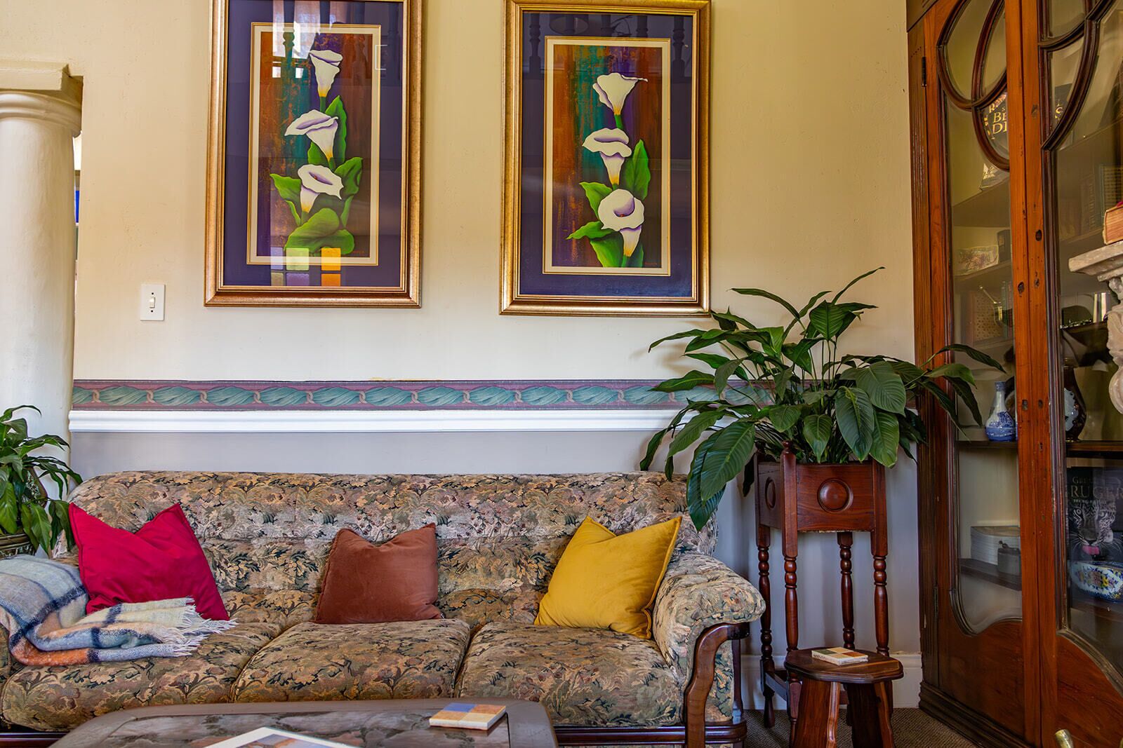 A living room with a patterned sofa, two framed calla lilies, and a wooden sideboard.