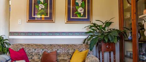 A living room with a patterned sofa, two framed calla lilies, and a wooden sideboard.