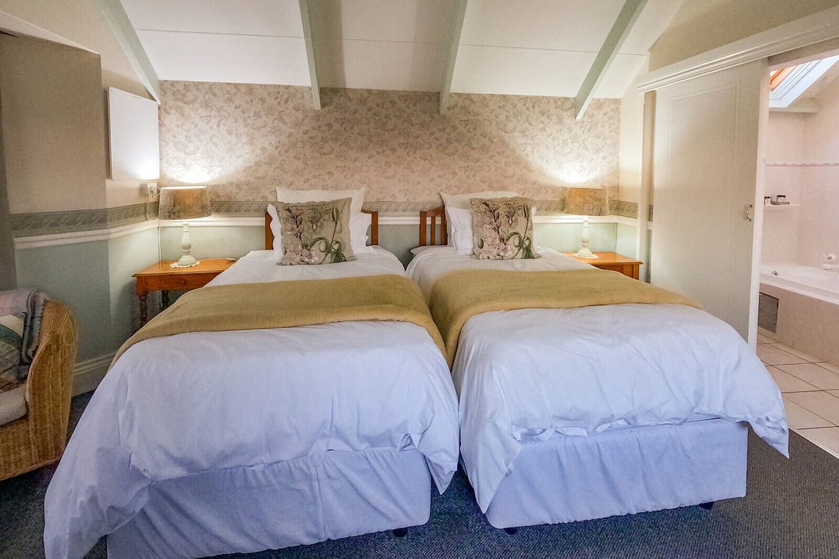 A double room with two beds, a nightstand, a lamp, and a view of a bathroom.