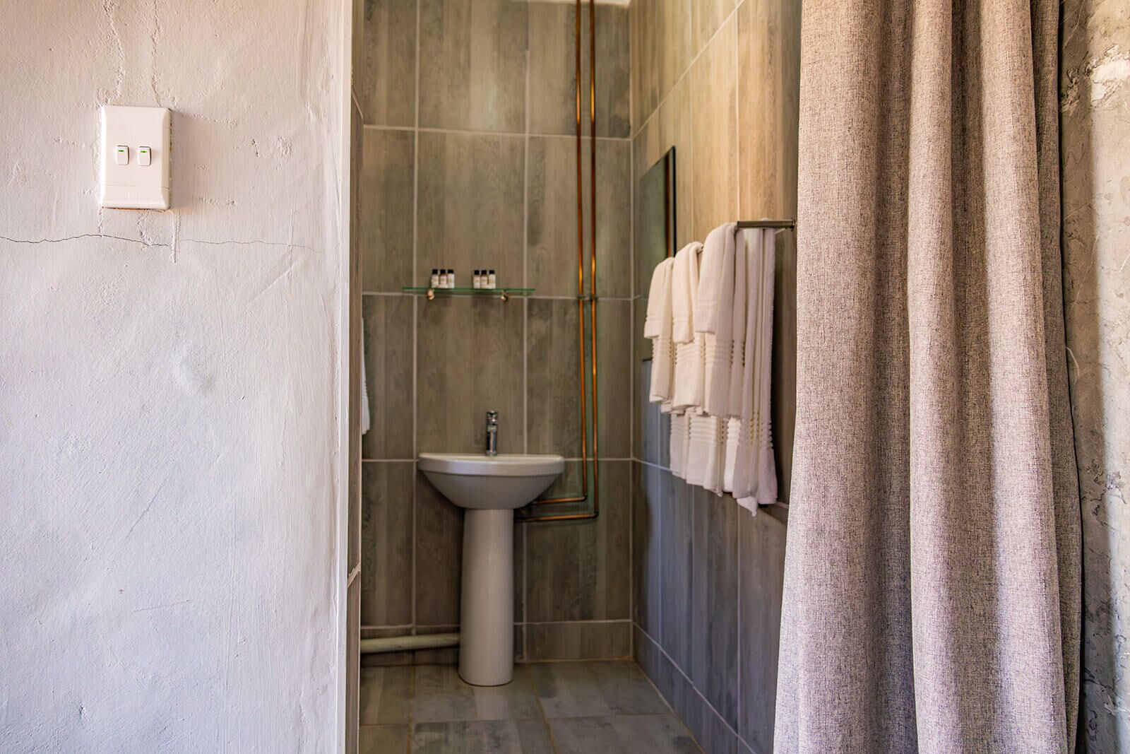 A bathroom with a pedestal sink, a glass shower enclosure, and a towel rack with multiple towels.