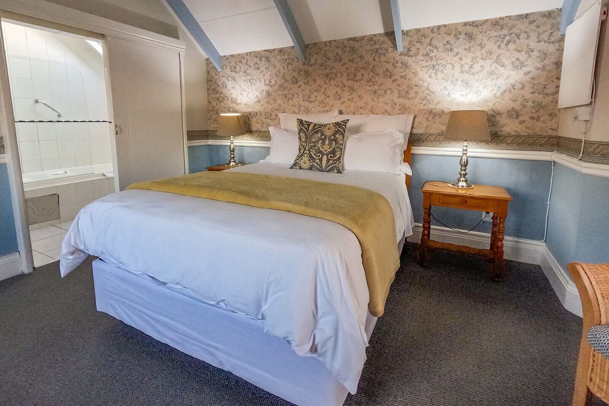 A bedroom with a bed, two bedside tables, a lamp, a wardrobe, and a bathroom with a shower.