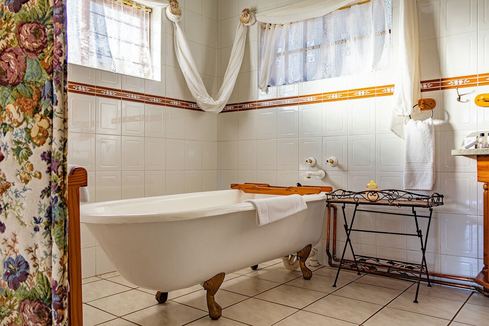 A bathroom with a freestanding bathtub, a wooden stool, a metal drying rack, and a tiled floor.